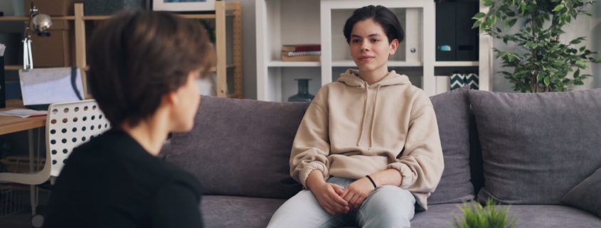 A clinician sitting with a client on a couch during a family-focused therapy session