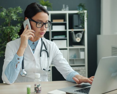 A physician working at a desk with laptop and phone — choosing a residential rehab program