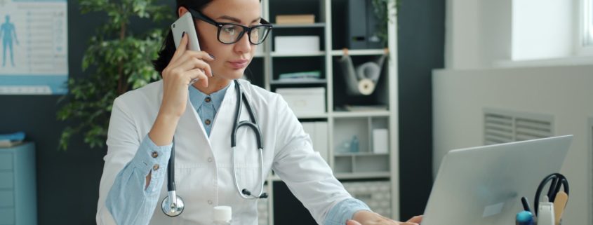 A physician working at a desk with laptop and phone — choosing a residential rehab program